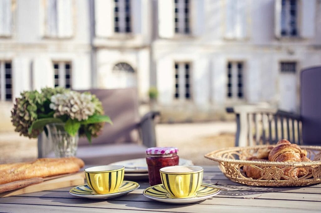 vintage coffee cups on outdoor breakfast table with croissants and baguette